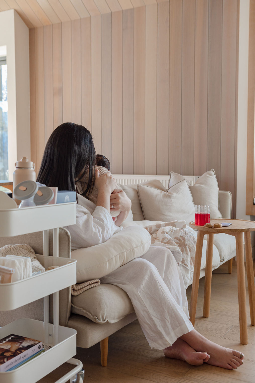 A woman is sitting on a white couch with a baby on her lap.