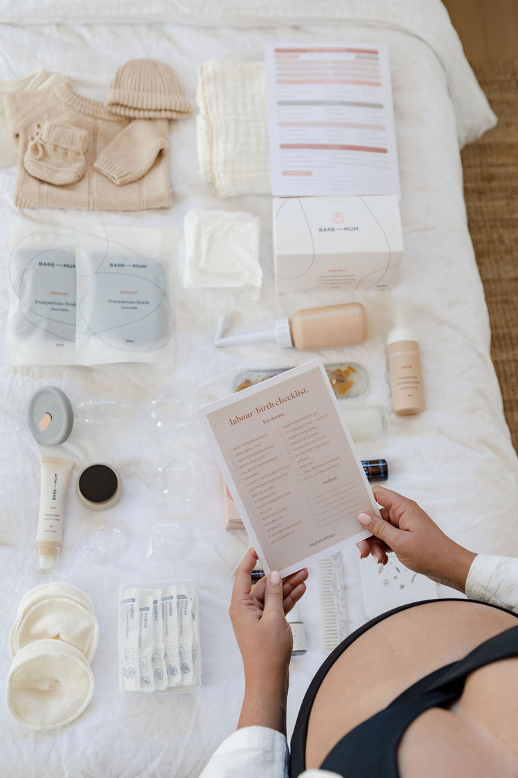 A pregnant woman is sitting on a bed with various items on it.